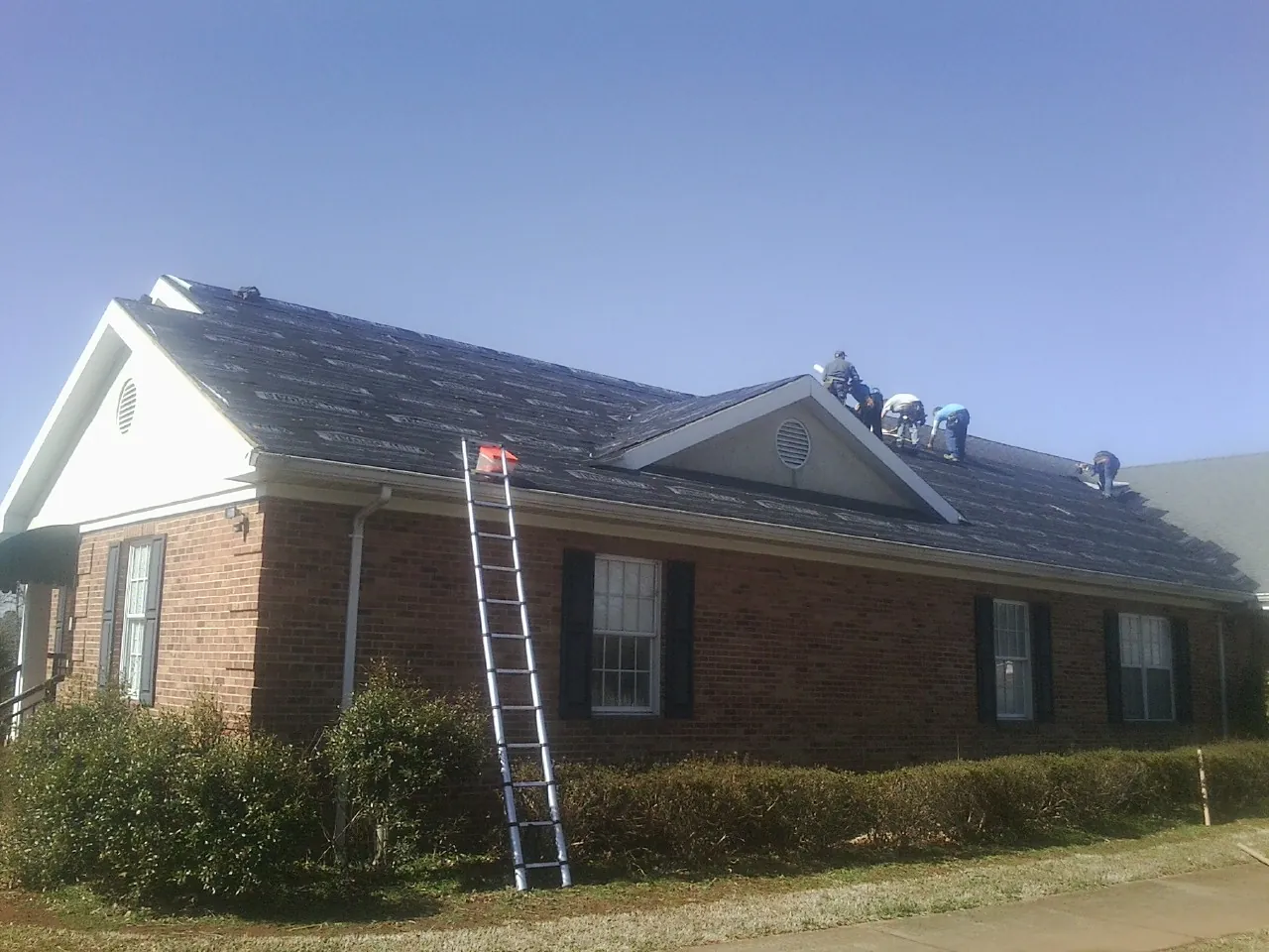 Crew tearing shingles off a brick ranch roof with a ladder set — Emergency Roof Repair work by our crew in Dale
