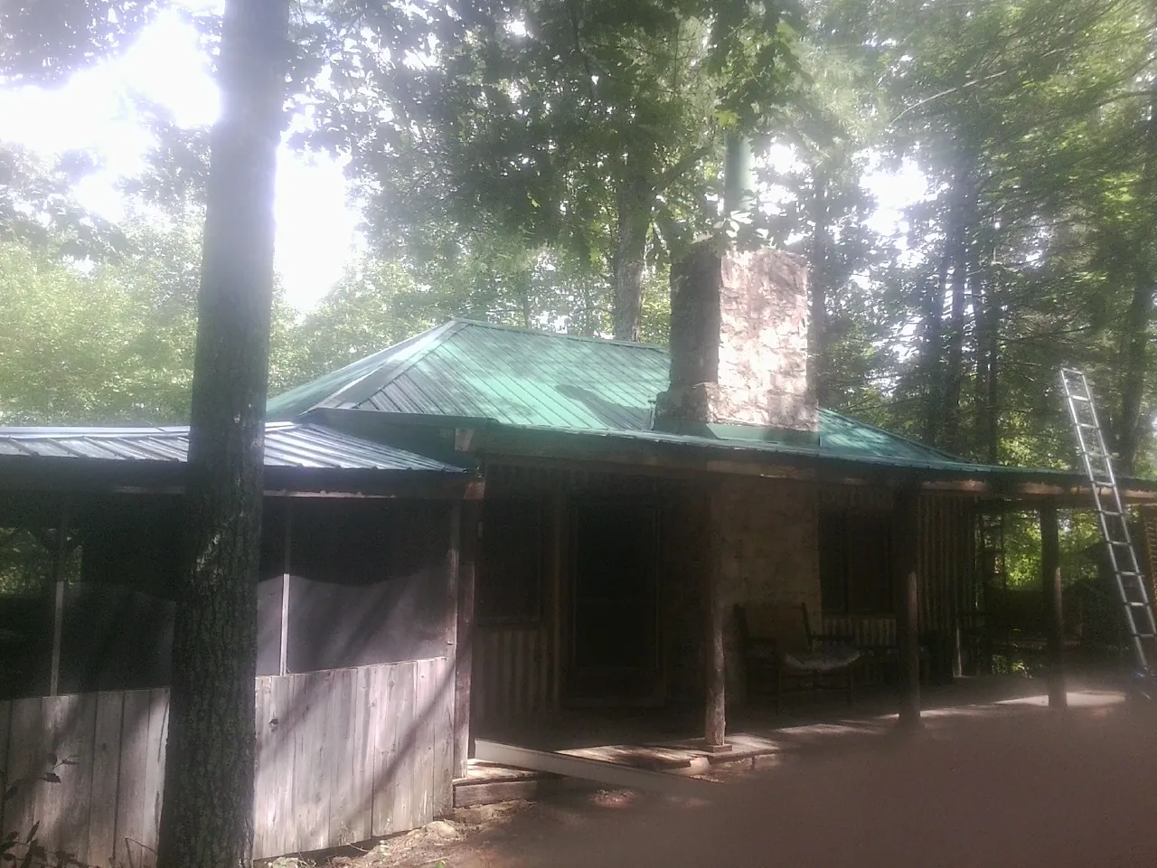 Green metal roof and stone chimney above a log cabin porch in Dale