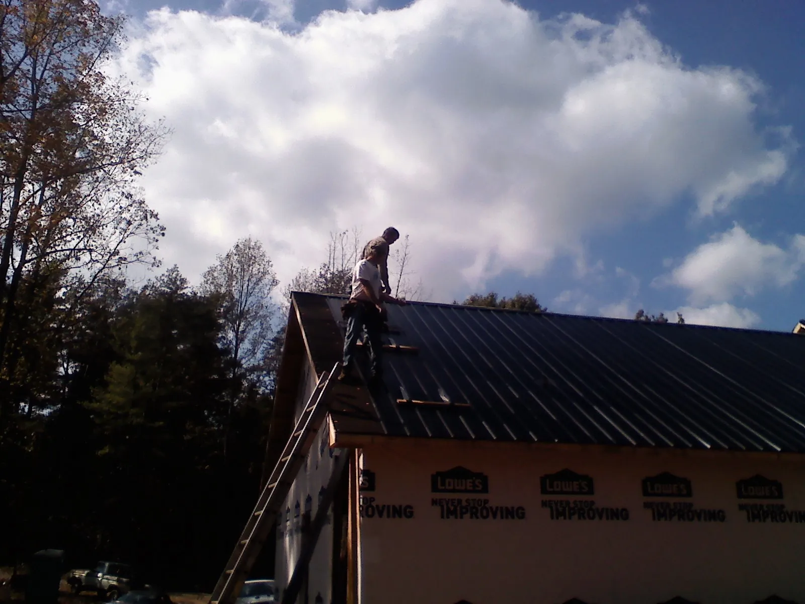 Roofer fastening dark metal panels high against a cloudy sky, from a Roof Inspection job in Dale