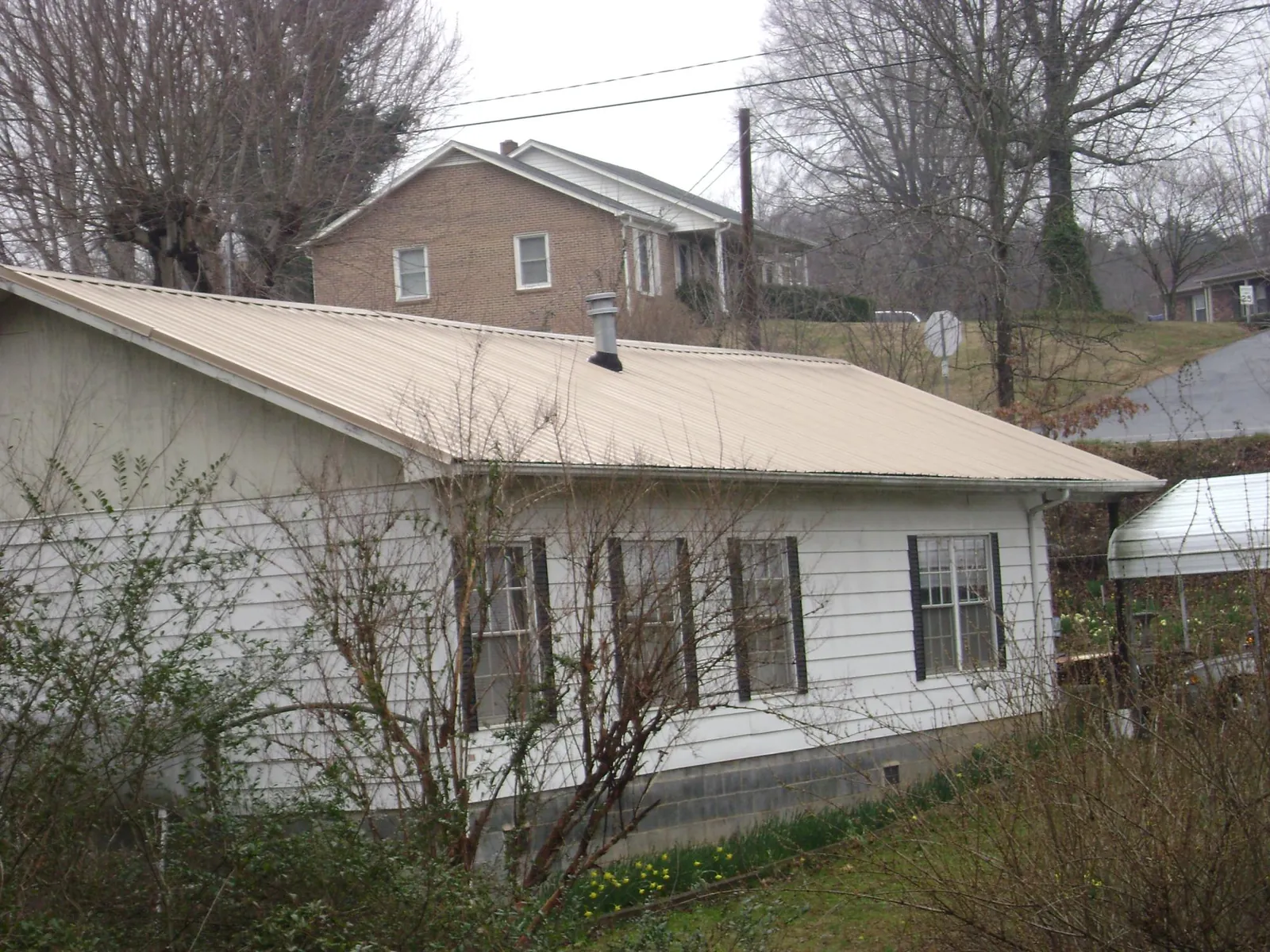 Tan metal roof on a white sided house set into a hillside — Commercial Roofing by Roofing Brothers in Dale